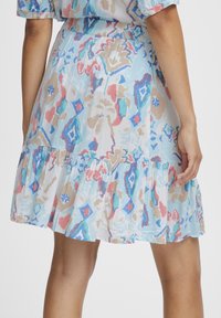 Robe courte, bleu clair, avec un ourlet à volants superposés. Présente un motif abstrait multicolore en rose, rouge, beige et turquoise. Tissu texturé.
