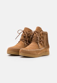 Semišové kotníkové boty v odstínu tan s třásňovým detailem, kulatou špičkou, šněrovacím designem, bílými švy a texturovanou gumovou podrážkou.