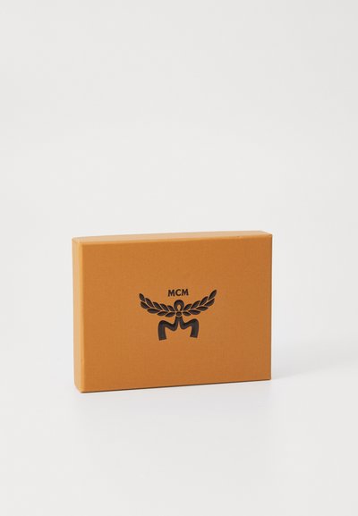 Oranssi suorakulmainen laatikko, jossa on sileä pinta, ja etupuolella musta painettu logo ja koristeellinen emblem.