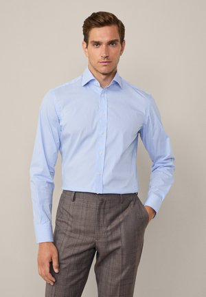 Chemise à manches longues bleu clair avec de fines rayures blanches. Dotée d'un col classique et d'une fermeture à boutons sur le devant, associée à un pantalon brun à motifs.