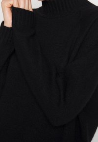 Maglione nero con colletto alto e polsini a coste. La texture è morbida e lavorata a maglia, con una vestibilità rilassata e dettagli minimi.