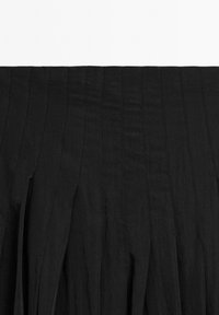 Black skirt with vertical pleats, made from lightweight fabric. Features a textured finish and a smooth waistband, offering a flowing design.