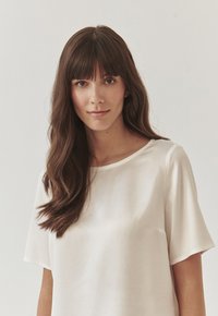 Blusa color crema con una textura suave, mangas cortas y cuello redondo. Presenta un ajuste holgado y un diseño minimalista.