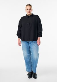 Crni pulover s ovratnikom, s gumbima i oversized krojem. Uparen s svijetloplavim, ležernim trapericama i crnim čizmama do gležnja.