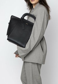 Black leather tote bag with a structured design, featuring a top handle, textured finish, and a small tag attached.