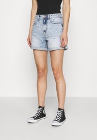 Světle modré denimové kraťasy s ohrnutým lemem, mírně poškozené a s klasickým pět pocket designem, spárované s černými vysokými teniskami.
