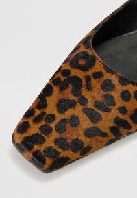 Leopard print flat shoe featuring a square toe, smooth caramel-colored material, and textured black spots on a light brown background.