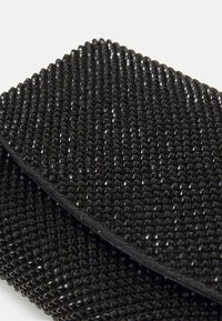 Zbliżenie na czarną prostokątną kopertówkę pokrytą małymi, błyszczącymi czarnymi koralikami ułożonymi w wzór siatki.