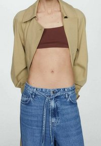 Giacca beige sopra un top corto marrone abbinato a jeans in denim azzurri a vita alta con chiusura a coulisse e bottone.