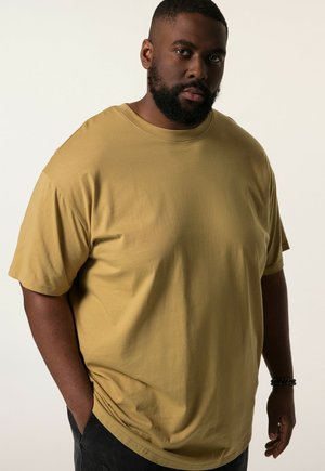 Khaki korte mouwen t-shirt van zachte stof, met een relaxte pasvorm en ronde halslijn, gedragen door een man met een baard, met zijn handen in zijn zakken.