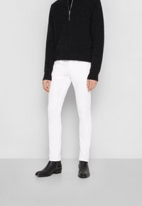 Suéter negro con cuello de cremallera, combinado con jeans ajustados blancos y botines negros. Las texturas suaves y los colores contrastantes crean un aspecto moderno.