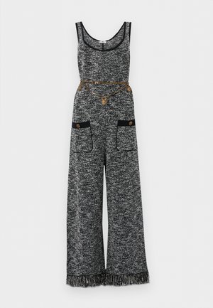 Αμάνικη ολόσωμη φόρμα σε ασπρόμαυρη υφή με φαρδιές παντελόνες, εμπρόσθιες τσέπες με κουμπιά, τελείωμα με φουντάκια και ζώνη από χρυσή αλυσίδα με μετάλλια.