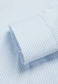 Tela de camisa a rayas azul claro y blanca con un puño doblado, que presenta una textura fina y detalles de costura precisos.