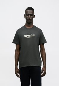 Ciemnoszara bawełniana koszulka z białym nadrukiem tekstowym "Calvin Klein New York City Since 1968". Krótkie rękawy, okrągły dekolt.