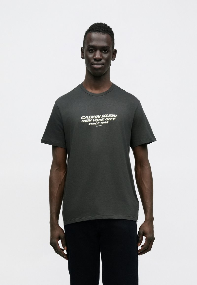 Ciemnoszara bawełniana koszulka z białym nadrukiem tekstowym "Calvin Klein New York City Since 1968". Krótkie rękawy, okrągły dekolt.