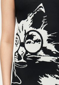 Μαύρο και άσπρο πλεκτό ύφασμα που δείχνει μια κοντινή λήψη μιας γάτας που φοράει στρογγυλά γυαλιά σε αμάνικο τοπ.