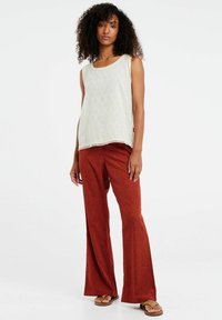 Top senza maniche di colore chiaro con motivo texturizzato; pantaloni a palazzo rossi con stampa a piccoli pois neri; indossato con sandali bassi.