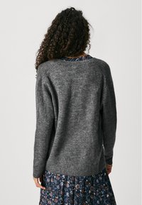 Grauer Strickpullover mit rundem Ausschnitt, geripptem Saum und langen Ärmeln, kombiniert mit einem rock mit floralem Muster. Weiche Textur.