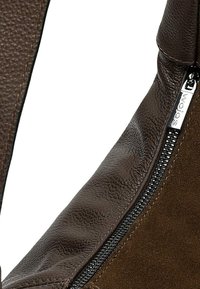 Bruine leren en suède handtas met een gestructureerde afwerking, voorzien van een ritssluiting en een afgeronde vorm. Stikdetails langs de rand.