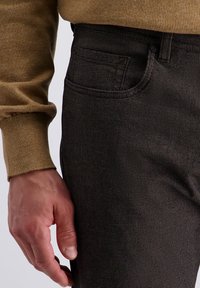 Un pantalon texturé marron présente un motif à carreaux subtil, une poche avant et une coupe classique. Le tissu a une apparence lisse.