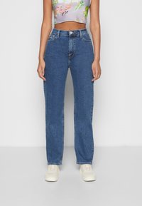 Vaqueros de tiro alto azul claro de denim, con un diseño de pierna recta, un ligero desgarbado y bolsillos frontales. Se llevan con un top corto floral.