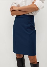 Jupe navy à coupe droite, tissu lisse et taille cintrée. Associée à une chemise blanche à boutons et des bottes noires hautes.