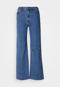 Jeans de perna larga em denim azul médio, apresentando uma cintura alta, bolsos frontais e um detalhe de remendo desgastado no joelho esquerdo.