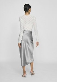 Haut à manches longues blanc avec un motif en losanges texturé, associé à une jupe en satin argenté lisse, présentant un ourlet asymétrique.