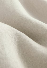 Tessuto in lino beige chiaro con una superficie liscia e testurizzata. Motivo di trama sottile visibile, creando una caduta morbida.