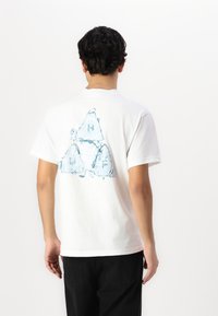 Balta medvilninė marškinė su mėlynu geometriniu piešiniu ant nugaros. Trumpomis rankovėmis ir klasikinio apykaklės dizainu. Laisvas stilius.