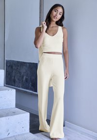 Helles gelbes geripptes Strick-Zweiteiler-Set mit einem ärmellosen Crop-Top und weit geschnittenen Hosen aus einem weichen Material.