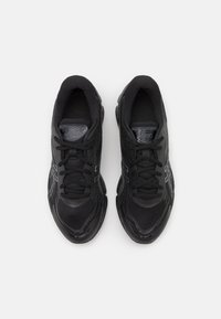 Chaussures de sport noires avec une tige en maille texturée, lacets plats et une semelle rembourrée. Présente des accents réfléchissants et un logo sur la languette.