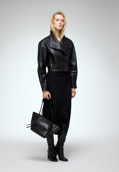 Černá kožená motocyklová bunda, upnutá černá sukně s rozparkem, černé kozačky do kolen a černá taška na rameno se dvěma uchy.