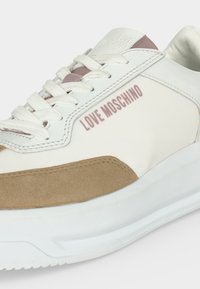 Baskets Love Moschino blanches et beiges avec des lacets blancs et un logo sur le côté et la languette, présentées en gros plan.