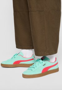 Sneakers w kolorze akwamarynu z zamszu z różowymi akcentami, sznurowany model, z brązową gumową podeszwą, w zestawie z białymi skarpetkami i brązowymi szerokimi spodniami.