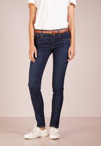 Mörk tvättade jeans med slim fit, försedda med ett brunt läderbälte, fem-ficksdesign och minimal sömnad. Tillsammans med vita sneakers.