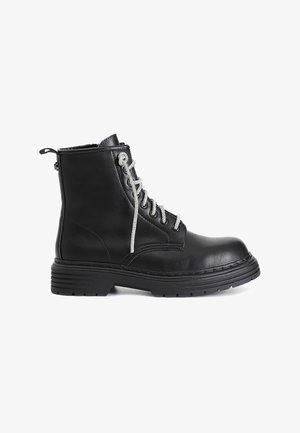 Stivale alla caviglia in pelle nera con lacci argentati, dettaglio con zip sul retro, suola robusta e sottili accenti di cucitura. Stile classico da combattimento.