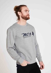 Grå sweatshirt lavet af blødt stof, med lange ærmer, en rund hals og et mørkeblåt logo på forsiden.
