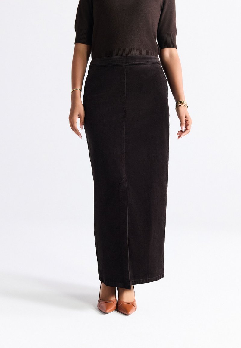 Black corduroy maxi skirt with a straight silhouette, featuring seam details and a high waist, paired with brown pointed-toe heels.