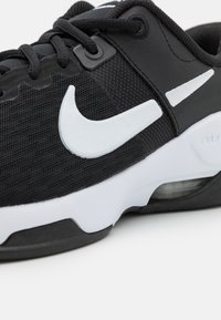 Black athletic shoe with mesh upper, white Nike swoosh, white accents, and visible air cushion in heel. Black rubber sole with textured pattern.