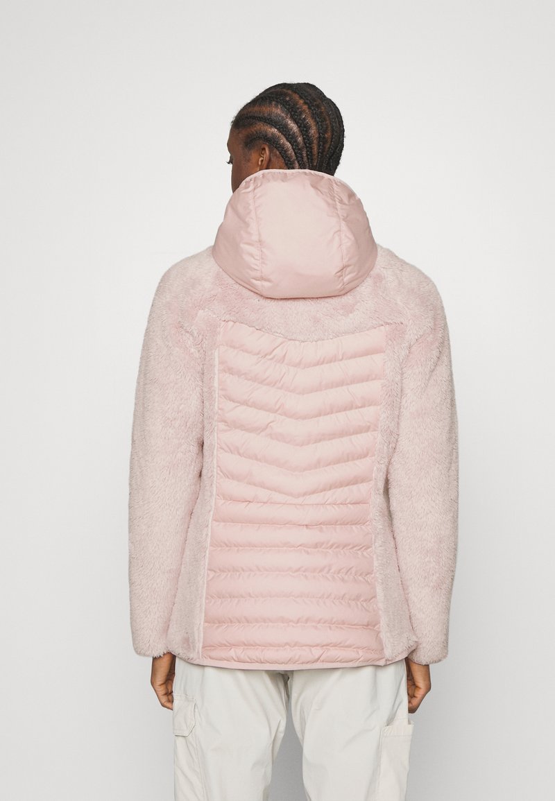 Rosa Kunstpelzjacke mit einem gepolsterten, gesteppten Rücken und Kapuze. Die Ärmel sind flauschig und schaffen einen texturierten Kontrast. Weiches, plüschiges Gefühl.
