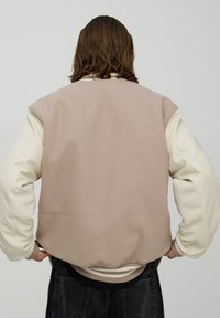 Reversyjna kurtka bomberka z beżowym plecakiem z czesanki i kremowymi rękawami z syntetycznej skóry. Kasmikowe ściągacze u dołu i na mankietach.