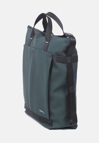 Groene waterdichte totebag met zwarte nylon handvatten, een voorvak en een ritsafsluiting. Zachte textuur en gestructureerde vorm.