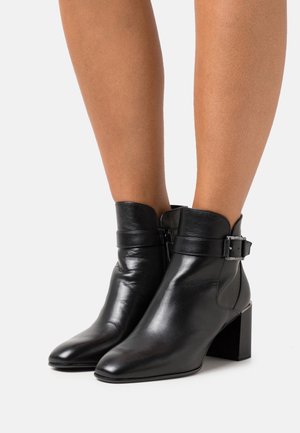 Botines de cuero negro con puntera en punta, tacón cuadrado y detalle de hebilla lateral. Textura suave y altura por encima del tobillo.