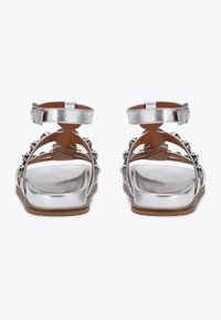 Sandali piatti argento con cinturino alla caviglia regolabile, parte anteriore decorata e soletta in pelle liscia con suola esterna marrone texturizzata.