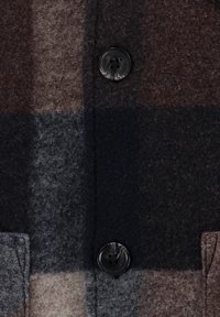 Kabát z vlněné směsi s velkým kostkovaným vzorem v odstínech hnědé, šedé a námořnické modři, s dvěma černými knoflíky a texturovaným povrchem.