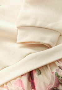 Kreemivärvi sweatshirt kangas ribbed kinnastega, kihtidena läbipaistva seeliku kohal, millel on pehme roosa ja rohelise tooni lillemuster.