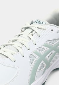Zapatilla deportiva blanca con paneles de malla, acentos verdes y superposiciones texturizadas. Presenta cordones planos y un diseño de punta curva.