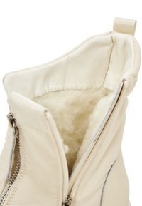 Bocanci de gleznă din piele crem, cu închidere cu fermoar. Interior moale, pufoasă și un tab cu buclă în partea de sus. Textură netedă și design elegant.