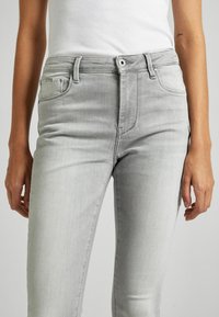Jeans de mezclilla gris claro con un corte ajustado, que cuentan con un diseño tradicional de cinco bolsillos, trabillas para cinturón y un cierre de botón simple.